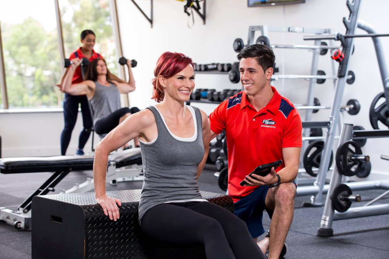 Fit people enjoying a workout. A Vision PT staff member looks on holding a tablet.